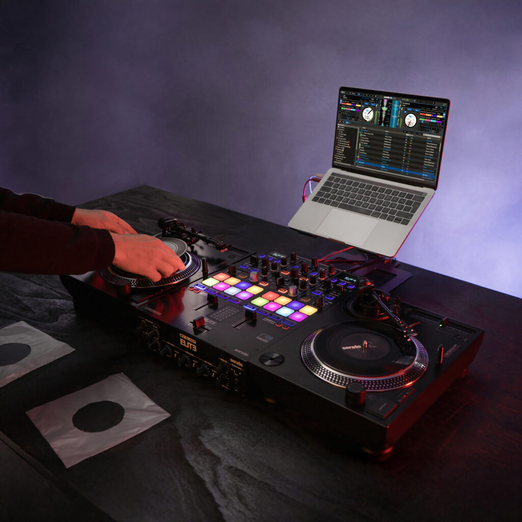 DJ performing on dual Reloop RP-7 turntables with a Reloop ELITE mixer and Serato DJ Pro laptop setup, showcasing a modern DVS workflow for 7-inch control vinyl.